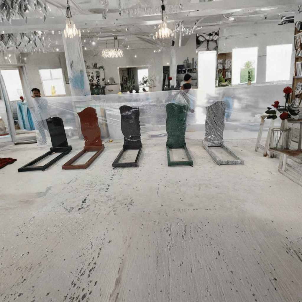 A workshop display of five complete upright granite monuments with matching memorial kerb sets, showcasing premium natural stone colors including absolute black, imperial red, paradiso, rainforest green, and viscon white.