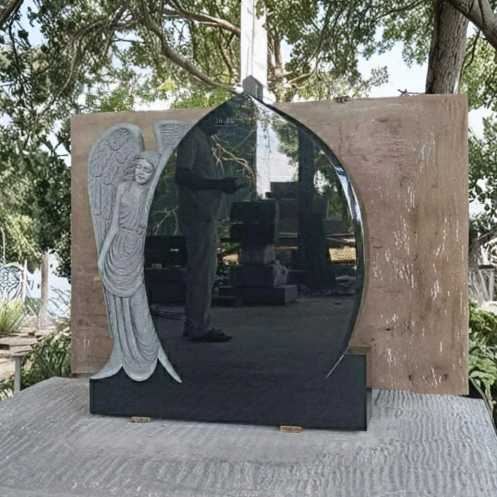 High-polished black granite upright memorial headstone featuring an intricately hand-sculpted angel in a light grey finish on the left edge, placed on a solid black granite base
