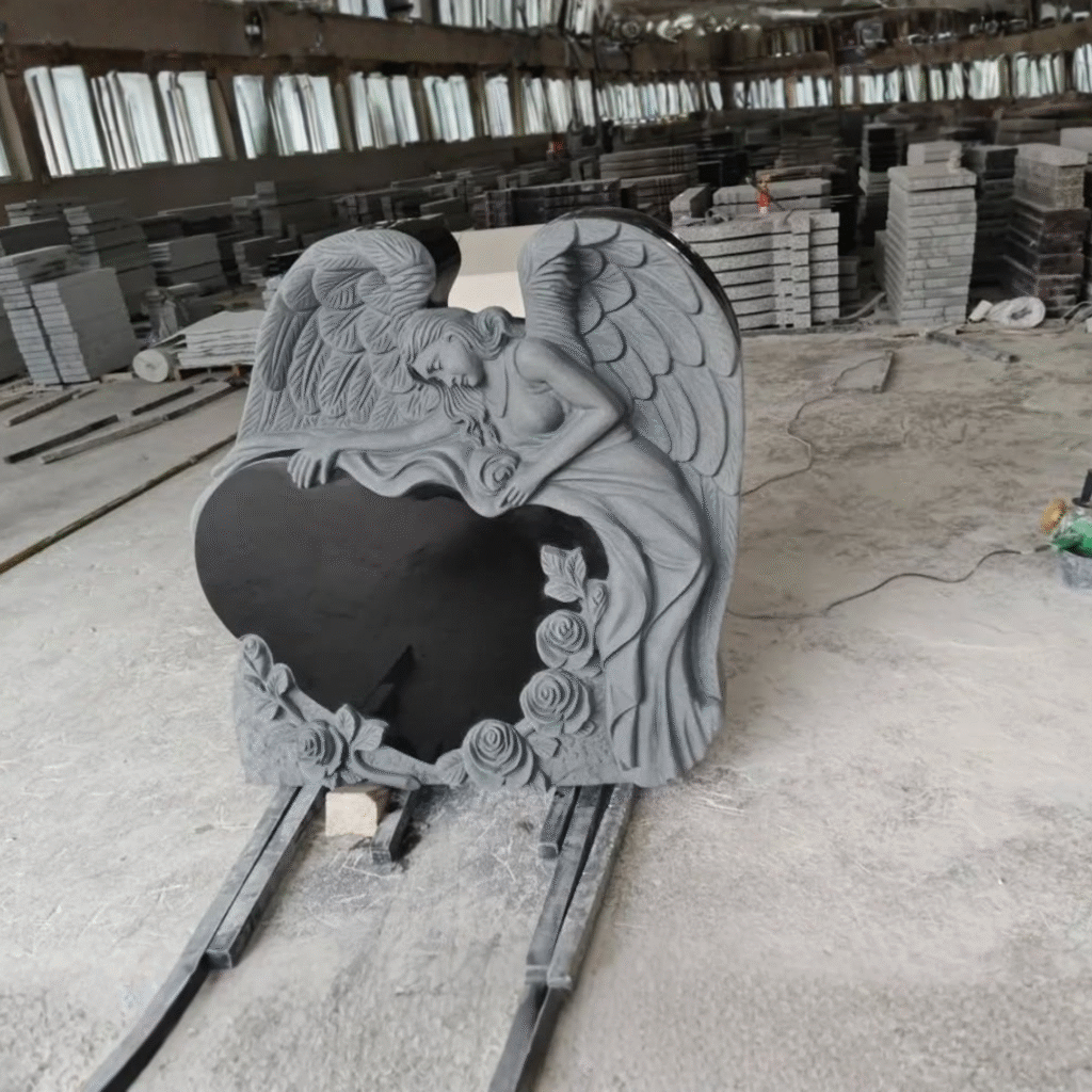 Intricately hand-carved grey frosted angel leaning over a high-polished black granite heart, featuring detailed rose blossoms at the base